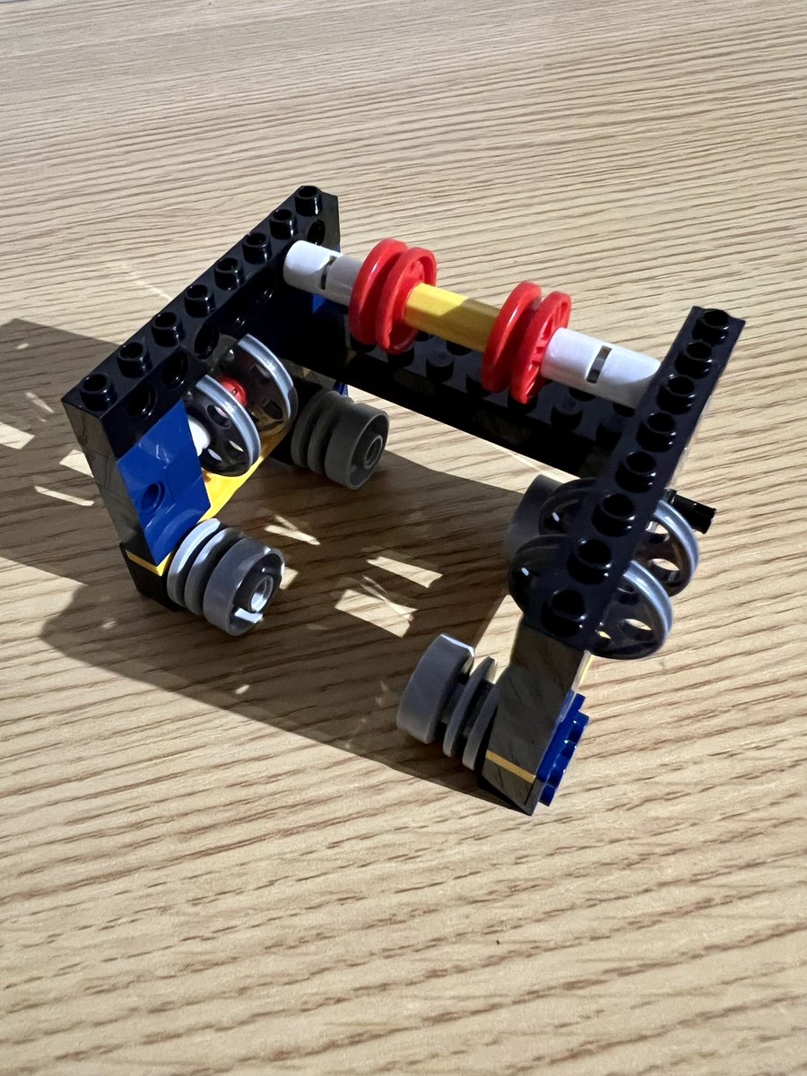A small lego structure with four wheels on the bottom, two sets of two thinner wheels in the middle, and two red wheels on the top.