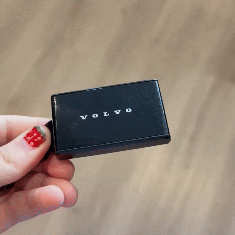 A black volvo key fob being held and turned over to show that there are no buttons on any side of it.