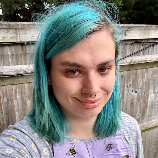 A photo of Liv, who is white and has shoulder length teal hair, a septum piercing, and a nose ring. She's wearing a purple dress covered in bees.